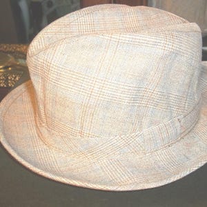 May include: A light brown fedora hat with a plaid pattern. The hat has a wide brim and a slightly indented crown.