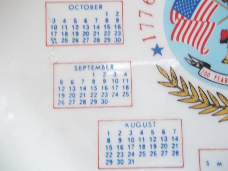 May include: White decorative item with calendar months of August, September, and October. The design includes the American flag and the text "1776" and "200 YEARS". The calendar dates are in blue.