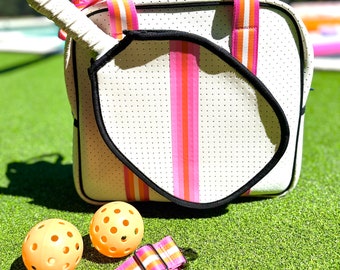 May include: White and black paddle ball set with a pink and orange striped bag. The bag has a handle and a shoulder strap. The set includes two orange paddle balls.