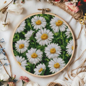 May include: A close-up of a white embroidery hoop with a floral design of white daisies on a green background.