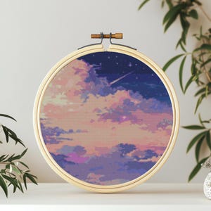 Peut inclure: Un cercle de broderie en bois rond avec un motif de point de croix d'un ciel rose et violet avec une étoile filante. Le ciel est rempli de nuages et d'étoiles.
