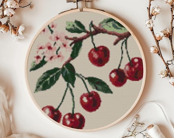 May include: A cross-stitch embroidery hoop featuring a design of a cherry blossom branch with red cherries hanging from it. The background is cream coloured.