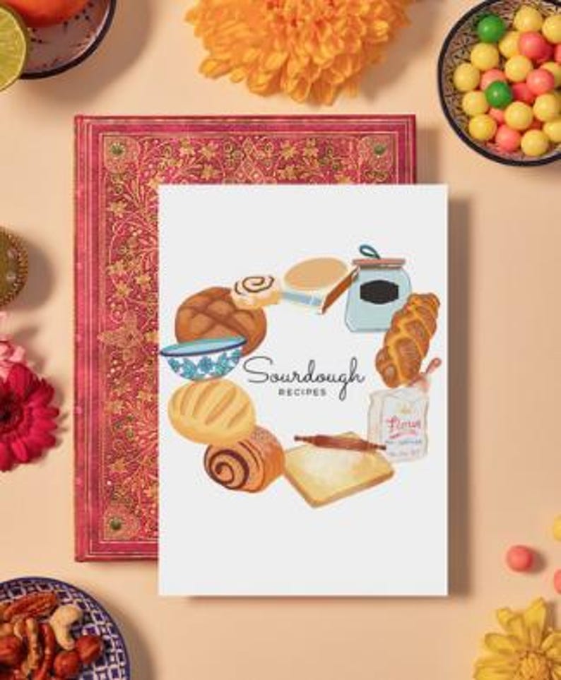May include: A white card with a circle of illustrated sourdough bread, rolls, and a bowl of dough. The text "Sourdough Recipes" is in the center of the circle.