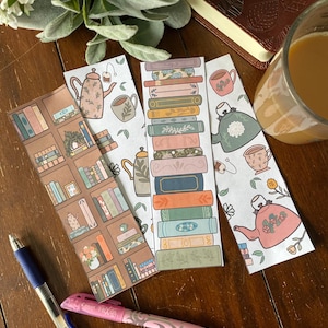 May include: Four printable bookmarks featuring a teacup, teapot, and stacks of books. The bookmarks are printed on white paper with brown, green, and pink accents.