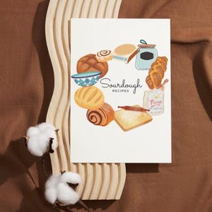 May include: A white card with a circle of sourdough bread, a bowl, a jar, a rolling pin, and a bag of flour. The text "Sourdough Recipes" is in the center of the card.