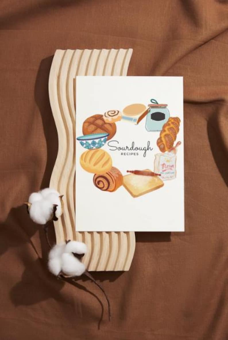 May include: A white card with a circle of sourdough bread, a bowl, a jar, a rolling pin, and a bag of flour. The text "Sourdough Recipes" is in the center of the card.
