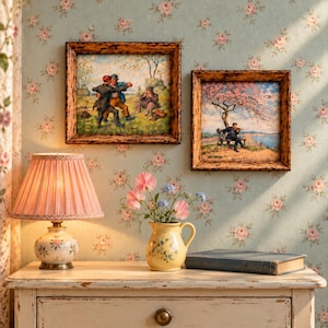 May include: Two framed landscape paintings featuring figures in a field and by a lake, a pink pleated lamp with a floral base, a yellow ceramic pitcher with blue and pink flowers, and a closed book on a white wooden drawer unit.