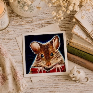 May include: A square greeting card featuring a detailed illustration of a brown mouse with large ears reading a red book against a dark blue background. The mouse has visible whiskers and paws resting on the open pages of the book.