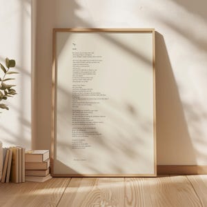Könnte beinhalten: Gerahmter Druck mit dem Gedicht "Steps" von Frank O'Hara. Der schwarze Text befindet sich auf cremefarbenem Hintergrund, in einem hellen Holzrahmen. Der Druck liegt auf einer Holzoberfläche, mit Büchern und einer Pflanze.