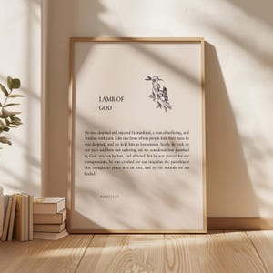 Puede incluir: Una impresión enmarcada con el texto "LAMB OF GOD" y una ilustración floral. La impresión presenta un pasaje de Isaías 53:3-5. El marco es de color marrón claro y el fondo es de un beige neutro.