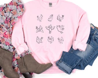 May include: A pink sweatshirt with a black and white graphic of nine birds. The birds are in various poses, some are flying, some are perched, and some are singing.