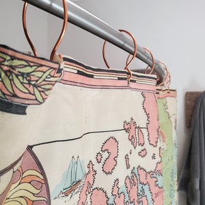 May include: A shower curtain with a map design featuring pink and blue islands, a sailboat, and the word "Devon" printed on the curtain. The curtain is hung on a silver shower rod with copper shower curtain rings.