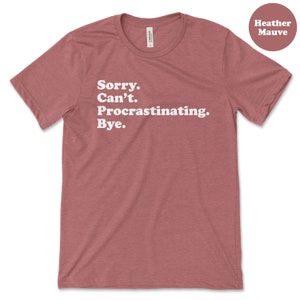May include: Heather mauve t-shirt with white text that reads "Sorry. Can't. Procrastinating. Bye."
