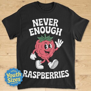 May include: Black t-shirt with the text "NEVER ENOUGH RASPBERRIES" in white. A cartoon raspberry character with a smiling face and waving hand is featured in the center. The shirt also has a "Youth Sizes" badge.