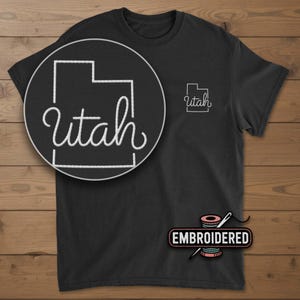 May include: Black t-shirt with a white embroidered outline of the state of Utah and the word "Utah" in a cursive font. A close-up shows the design in detail. The word "Embroidered" is below the design.