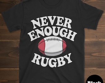 May include: Black t-shirt featuring the white text "NEVER ENOUGH RUGBY" with a red and white rugby ball graphic. The shirt has a crew neck and short sleeves. The word "Black" is in a black circle at the bottom right.