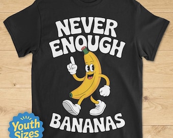 Op de afbeelding: Zwart T-shirt met de witte tekst "NEVER ENOUGH BANANAS". Een cartoon banaan karakter met een lachend gezicht, witte handschoenen en schoenen is afgebeeld. Een blauw en geel "Youth Sizes" badge staat linksonder.