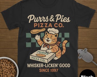 Pode incluir: Camiseta preta com um design de gato de desenho animado como chef. A camiseta mostra o texto "Purrs & Pies PIZZA CO." e "WHISKER-LICKEN' GOOD SINCE 1997." Uma tigela de comida para gatos e um rato de brinquedo também são visíveis.