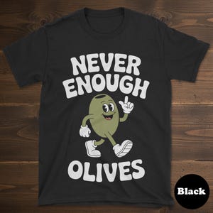 May include: Black t-shirt with the text "NEVER ENOUGH OLIVES" in white, above a cartoon olive character. The olive is green with white gloves and shoes, and is walking and pointing. The word "Black" is in a black circle at the bottom right.