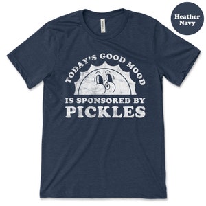 May include: A heather navy blue t-shirt with a white graphic of a smiling sun with the text "Today's Good Mood Is Sponsored By Pickles".