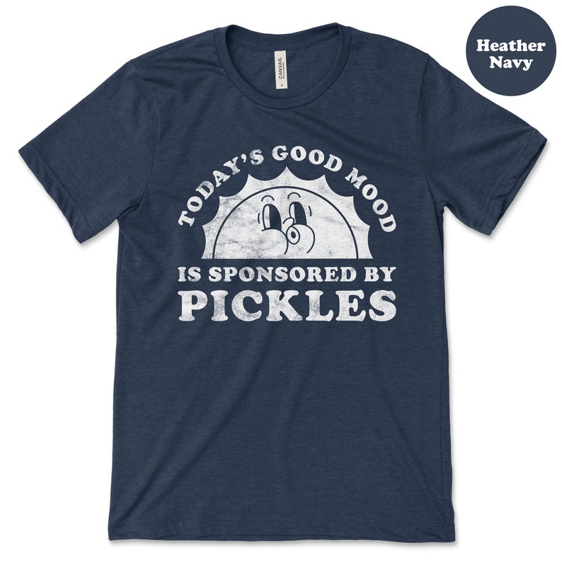 May include: A heather navy blue t-shirt with a white graphic of a smiling sun with the text "Today's Good Mood Is Sponsored By Pickles".