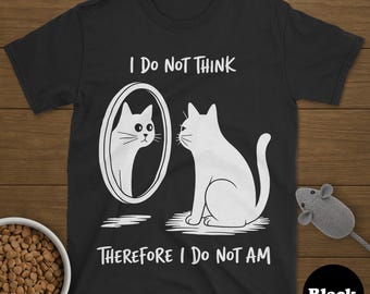 May include: Black t-shirt with a white cat design. The design features a cat looking in a mirror at its reflection, with the text "I DO NOT THINK THEREFORE I DO NOT AM". A bowl of cat food and a toy mouse are also visible.