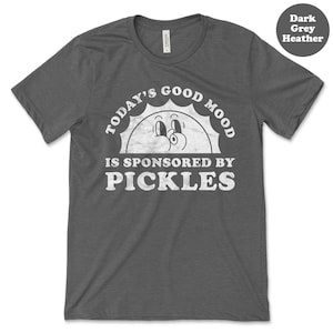 May include: Dark grey heather t-shirt with a white graphic of a smiling sun with the text "Today's Good Mood Is Sponsored By Pickles".