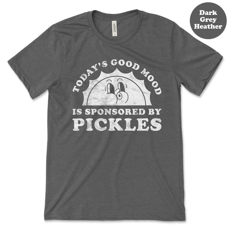 May include: Dark grey heather t-shirt with a white graphic of a smiling sun with the text "Today's Good Mood Is Sponsored By Pickles".