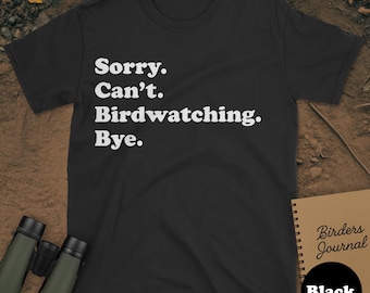 May include: Black t-shirt with the text "Sorry. Can't. Birdwatching. Bye." in white. The shirt is displayed with binoculars and a journal labeled "Birders Journal". A black circle with the word "Black" is also visible.