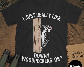 May include: Black t-shirt featuring the text "I JUST REALLY LIKE DOWNY WOODPECKERS, OK?" and a downy woodpecker graphic on a wooden post. A notebook with "Birders Journal" and the word "Black" is also visible.