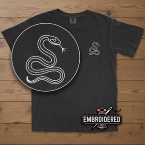 May include: Dark gray t-shirt with a white embroidered snake design. The shirt features a large snake illustration on the front and a smaller version on the chest. The word "EMBROIDERED" is printed on a label at the bottom.