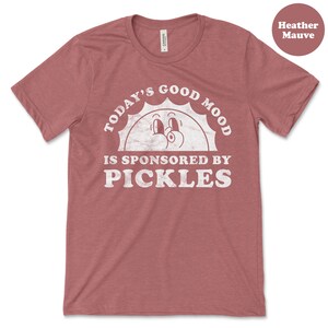 May include: Heather mauve t-shirt with a white graphic that says "Today's Good Mood Is Sponsored By Pickles" with a cartoon sun face.