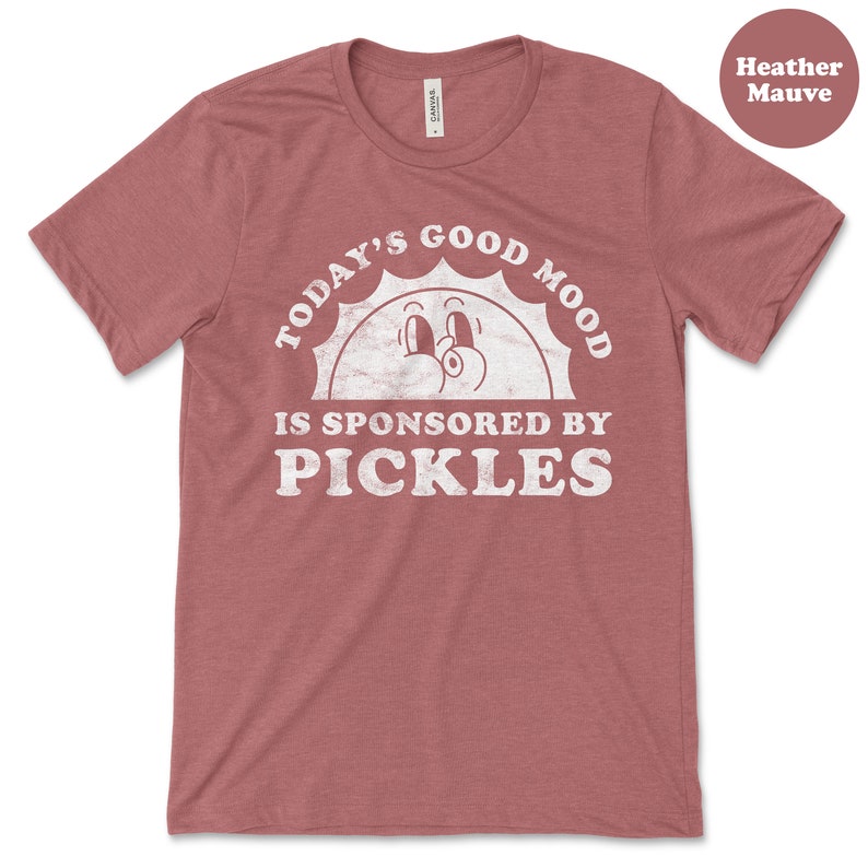 May include: Heather mauve t-shirt with a white graphic that says "Today's Good Mood Is Sponsored By Pickles" with a cartoon sun face.