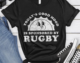 May include: Black t-shirt with a white graphic of a smiling sun with the text "Today's Good Mood Is Sponsored By Rugby".