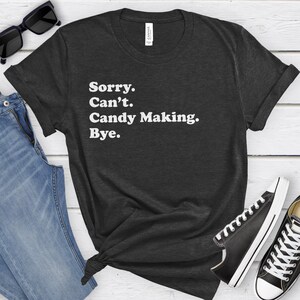May include: A dark grey t-shirt with white text that reads "Sorry. Can't. Candy Making. Bye."