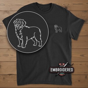 May include: Black t-shirt featuring a white embroidered outline of a dog, with a larger circular detail of the dog's image. The shirt also has a smaller embroidered dog image on the chest. The word "EMBROIDERED" is printed on the image.