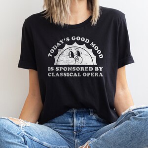 May include: Black t-shirt with a white graphic of a smiling sun with the text "Today's Good Mood Is Sponsored By Classical Opera."