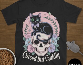 May include: Black t-shirt featuring a black cat with a bow tie sitting on a skull, surrounded by flowers. The text "Cursed But Cuddly" is printed below the skull. A black circle with the word "Black" is in the lower right corner.