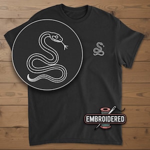 May include: Black t-shirt with a white embroidered snake design. The shirt features a larger snake illustration on the front and a smaller version on the chest. The word "EMBROIDERED" is displayed in a pink and white graphic.