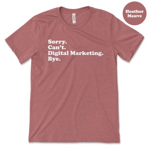 May include: Heather mauve t-shirt with the text "Sorry. Can't. Digital Marketing. Bye."