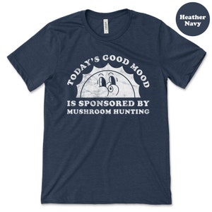 May include: A heather navy blue t-shirt with a white graphic of a smiling sun with the text "Today's Good Mood Is Sponsored By Mushroom Hunting".