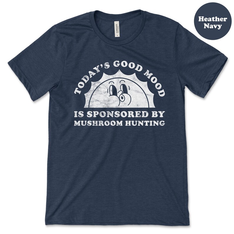 May include: A heather navy blue t-shirt with a white graphic of a smiling sun with the text "Today's Good Mood Is Sponsored By Mushroom Hunting".