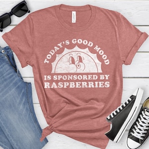 May include: A red t-shirt with a white graphic design. The graphic features a smiling sun with the text "Today's Good Mood Is Sponsored By Raspberries".