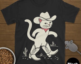 May include: Black t-shirt with a white cartoon cat in a cowboy hat, boots, and a red neckerchief, walking across a desert scene with cacti. A bowl of cat food and a toy mouse are also in the image.