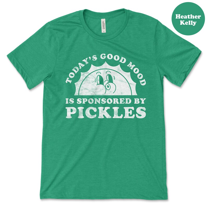 May include: Green t-shirt with a white graphic that says "Today's Good Mood Is Sponsored By Pickles". The graphic features a cartoon sun with a smiling face.