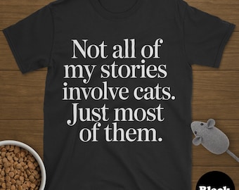 May include: Black t-shirt with the text "Not all of my stories involve cats. Just most of them." A small, gray toy mouse and a bowl of cat food are also visible. The word "Black" is in a black circle.