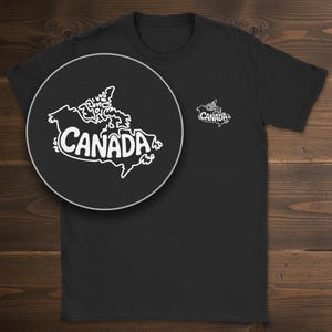 May include: A black short-sleeved t-shirt featuring a small white graphic on the left chest. The graphic displays a stylized outline map of Canada with the word CANADA written in bold, rounded white letters across the center of the map.