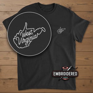 May include: Black t-shirt with a white embroidered outline of the state of West Virginia. The state's name is also embroidered in white. A smaller version of the design is on the left chest. The word "EMBROIDERED" is below the shirt.