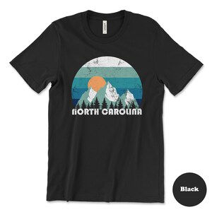 May include: Black t-shirt with a vintage-style graphic of mountains, a sun, and the text "NORTH CAROLINA".