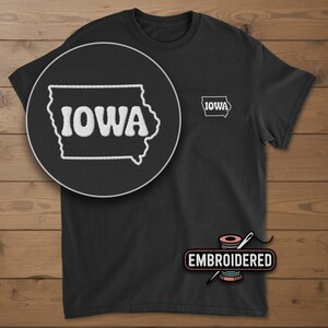 May include: Black t-shirt with an embroidered outline of the state of Iowa and the word "IOWA" in white. A smaller embroidered version of the design is on the chest. The word "EMBROIDERED" is also visible.